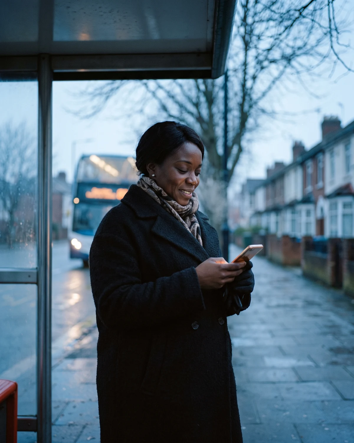 A woman at a UK bus stop in a winter coat, breath misting, the Insyt dashboard glowing on her phone.