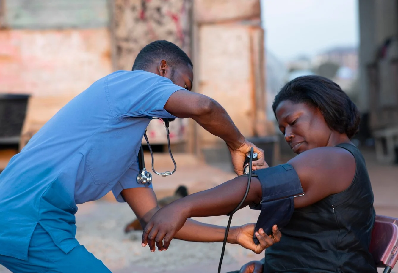 An Insyt care professional checks a woman’s blood pressure outdoors at her home, the cuff on her arm and the monitor in view.