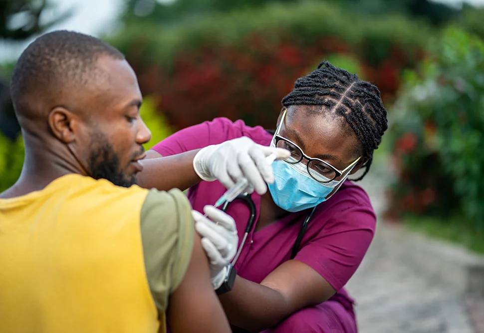 A gloved Insyt nurse gives an injection into a client’s upper arm outdoors at home, steady and precise.