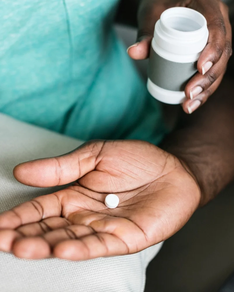 Medication held ready in hand beside its bottle, part of a supervised supplement and wellness plan.
