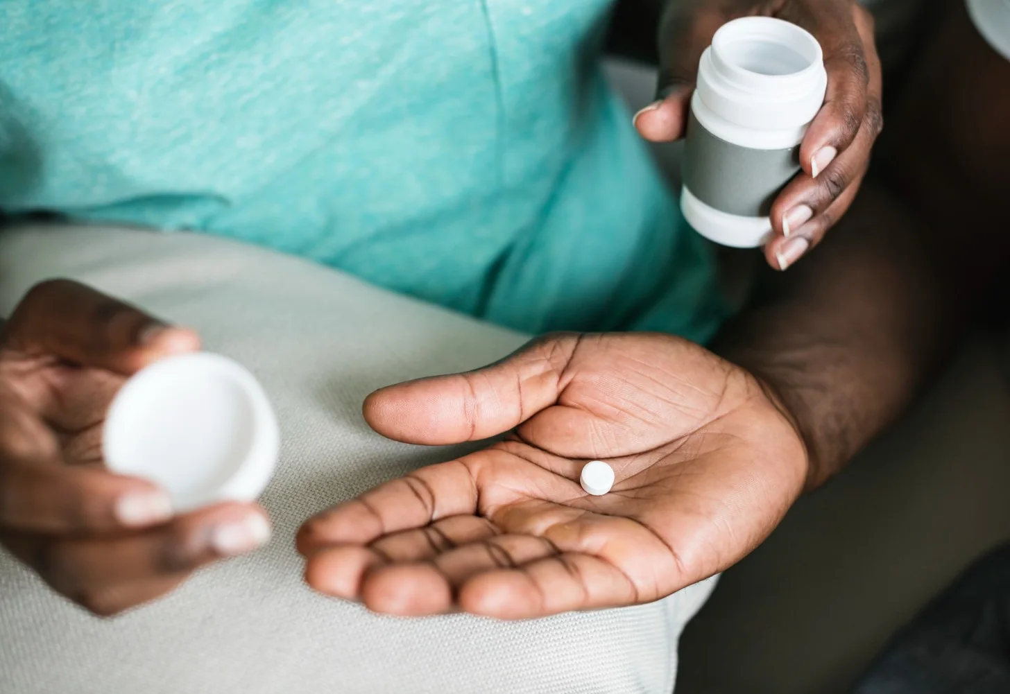 A hand holds a day’s medication beside an open pill bottle, part of a medication reminder round.